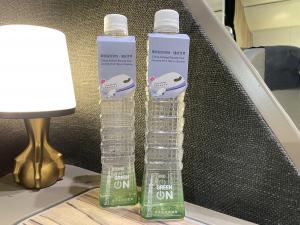 Two bottles of limited-edition “Taipei 101 Pure Water,” designed to resemble the Taipei 101 skyscraper, displayed beside a lamp in a premium airline cabin.