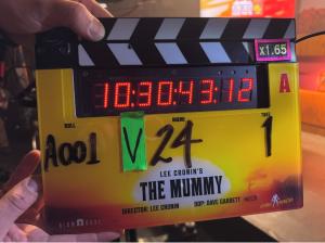 A digital film slate displaying the title “Lee Cronin’s The Mummy” with timing code and production notes, held by a crew member on set.