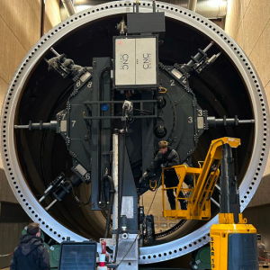 The tower flange is seen with CNC Onsite's machine mounted onto the flange. Two men are supervising the process. The size of the two  humans next to the flange reflects the proportion.