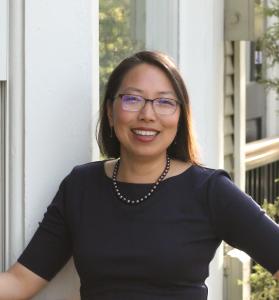Dr. Jackie Wirz, an educator, researcher and non-profit leader, stands outside wearing glasses and a black top