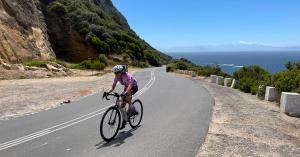 Gisa Göldner cycling on a coastal road with mountains and ocean in the background – symbolizing freedom, perspective, and inspiration