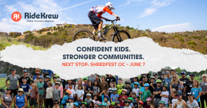 A youth mountain biker mid-air over a jump, with a crowd of kids and families gathered below, celebrating the upcoming SHREDFest OC event on June 7.