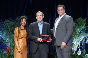 John A. Griswold, M.D., holds his ABA Lifetime Achievement Award plaque while standing onstage with the outgoing and incoming presidents of the American Burn Association.