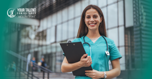 Female nurse standing confidently outside a healthcare facility, holding a clipboard and smiling.