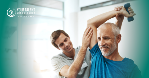 Male physiotherapist helping older man with shoulder exercise using a dumbbell in rehab setting.