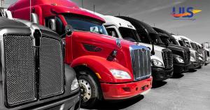 Row of semi-trucks with a vibrant red truck in the center, lined up in a transportation yard.