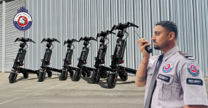 G Force Security guard communicates via radio while overseeing parked e-scooters near a secure facility.