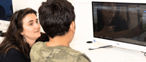 A child and an adult are engaged with a computer, focusing on the screen in a bright, modern workspace.