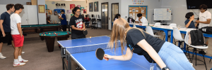 A group of students enjoys ping pong and pool in a vibrant activity room at a club, fostering camaraderie and fun.