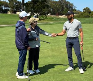 A young man and his father shaking hands with a special guest golfer on a golf course.