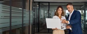 Two business professionals look intently at a laptop outside of an office building.