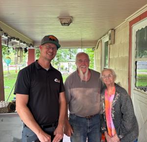 Rock Pest Control owner Matt Muller smiling alongside giveaway winner Leslie K. and his mother Barbara on the front porch of their Kansas home.