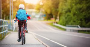 Image of young boy riding bike to school, riding on sidewalk
