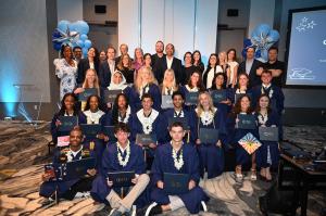 A few of ICL Academy's 2025 graduates, seated with blue robes and caps, holding their diplomas, as faculty members stand behind them, smiling.