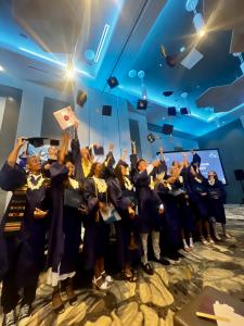 A few of ICL Academy's 2025 graduates wearing blue robes and smiling as they throw their caps into the air.