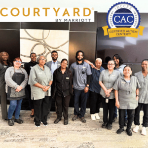A group of hotel staff members poses together in a modern lobby, featuring the Courtyard by Marriott and Certified Autism Center logos.