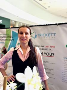 Portrait of Marinela Trickett, Registered Psychotherapist and Clinic Director at Trickett Psychotherapy and Counselling, standing in a  booth doing some community outreach to offer accessible psychotherapy services in Guelph.