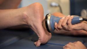 A provider is holding a 4 inch, conically shaped applicator to the bottom of a patient's foot. The patient is laying prone and only the providers arm is visible.