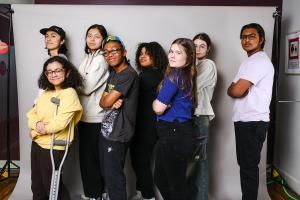 A group of diverse students, girls and boys, posing in a row, looking cool against a grey backdrop.