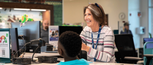 A librarian assists a child at a desk with computers and colorful decorations, promoting a welcoming learning environment.