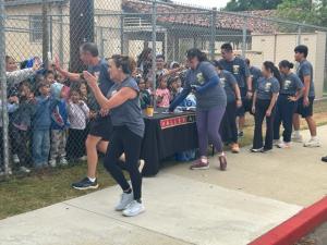 Valley Alarm table in front of O'Melveny School as officers and Torch Run participants grab drinks while high-fiving students behind the gate.