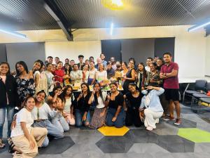 A large group of young adult graduates from the GEM Institute in Timor-Leste posing together in a classroom setting, smiling and celebrating.