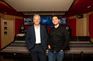 two men stand against recording console.