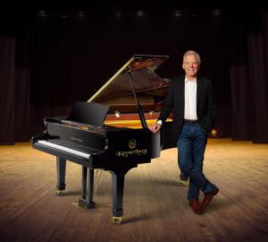 dark background, Ed in suit, standing by a Kayserburg piano