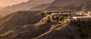 Desert hillside with a luxury resort nestled among palm trees, illuminated by warm sunset light, creating a tranquil atmosphere.