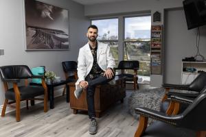 Dr. Robair Aldaya, wearing a white lab coat, sitting confidently in the modern waiting room of Million Dollar Smile dental office in San Diego, with natural light and a relaxed, stylish atmosphere.