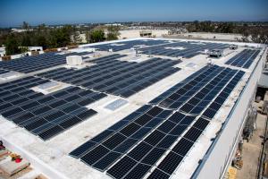 A photo of a large commercial solar system on a flat roof of a commercial building. The photo was taken from high above. There are hundreds or solar panels in this solar array.