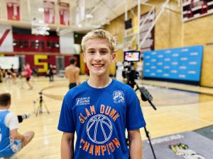 Nathan “Hoopin Nate” Kenney stands smiling in his Slam Dunk Champino t-shirt after winning the 8-foot low rim contest at Dunk Camp 2025 in Farmington, Utah, following his championship inverted scorpion dunk.