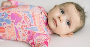 Baby lying on a bed wearing a pink western themed bamboo zipper pajama