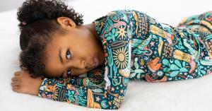 child lying on bed dressed in a dark green western cowboy themed bamboo pajama set