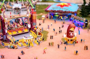Miniature funfair scene at Small Worlds Expo City Dubai with rides, a hot dog stand, and many tiny people, showcasing interactive elements and intricate model details.
