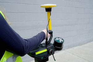 Closeup of an Exyn Nexys portable SLAM mapping unit integrated with Trimble DA2 GNSS Unit being handheld at a construction site.