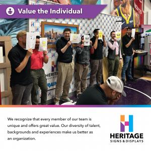 Heritage Signs & Displays employees holding emoji face drawings during a team-building activity at the Charlotte production facility.