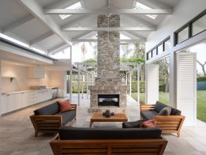 Open-plan outdoor living area with timber furniture, stone fireplace, vaulted ceiling, and louvre windows, designed by dion seminara architecture in Brisbane.