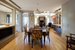Renovated dining and living area in an Indooroopilly post-war home featuring timber flooring, patterned upholstered chairs, pendant lighting, stone benchtops, and a built-in shelving unit with display lighting, designed by Dion Seminara Architecture.