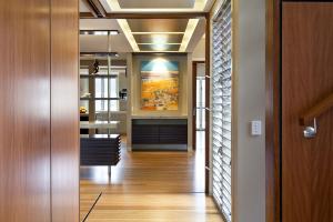 Entryway of renovated Indooroopilly post-war home with timber flooring, louvre windows, recessed ceiling lighting, and a feature artwork at the end of the hall.