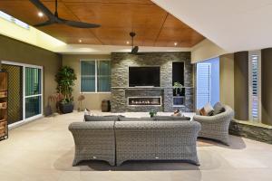 Covered outdoor living space in Yatala featuring stone fireplace, ceiling fans, wicker lounge seating, and built-in entertainment wall, designed by Dion Seminara Architecture.