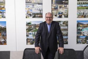 Dion Seminara standing in front of completed project images at the dion seminara architecture studio, representing flexible architectural service offerings.