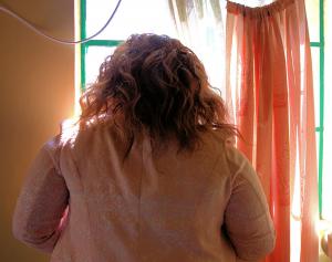 anonymous photo of a woman in a pink coat who is receiving support after experiencing commercial sexual exploitation, she is looking out a bright window
