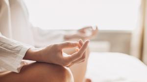 Woman sitting cross-legged in meditation pose with hands positioned in mudra gesture