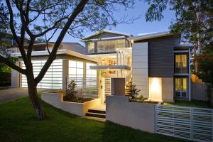 Exterior view of a renovated Indooroopilly post-war home at dusk, showcasing modern architectural updates with layered rooflines, large windows, and soft landscape lighting.
