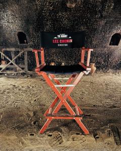 A director’s chair labeled “Lee Cronin – Director” with The Mummy reboot logo, placed on a sandy tomb-like set with carved ancient script on the walls behind it.