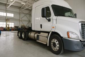 White American semi-truck inside a commercial truck repair shop with service equipment and tools in the background.