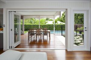 Bi-fold doors connecting a living area to a timber deck with outdoor dining and a view of a landscaped backyard and pool in Hawthorne by dion seminara architecture.