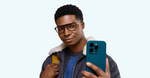 Man wearing Zenni Optical glasses, holding up a smartphone. He appears to be taking a selfie or browsing the app. Set against a light blue background.