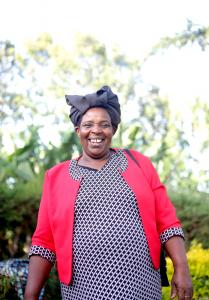 Esther, a woman coffee farmer in Kenya, smiling in a coffee field.